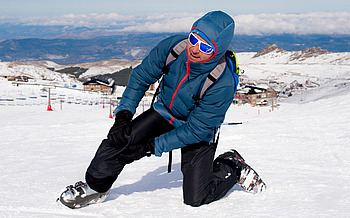 Mann hält schmerzendes Knie auf Skipiste nach Skiunfall