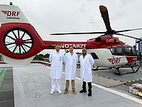 Dr. Blai und Dr. Khanyile stehen im Arztkittel vor einem Rettungshubschrauber