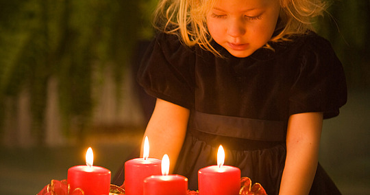 Mädchen blickt von oben auf die vier brennenden Kerzen des Adventskranzes