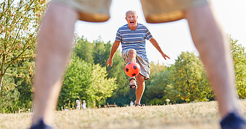 Älterer Mann spielt Fußball mit rotem Ball
