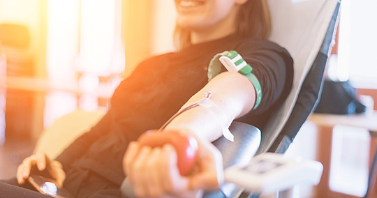 Junge lächelnde Frau beim Blutspenden mit Pumpball in der Hand