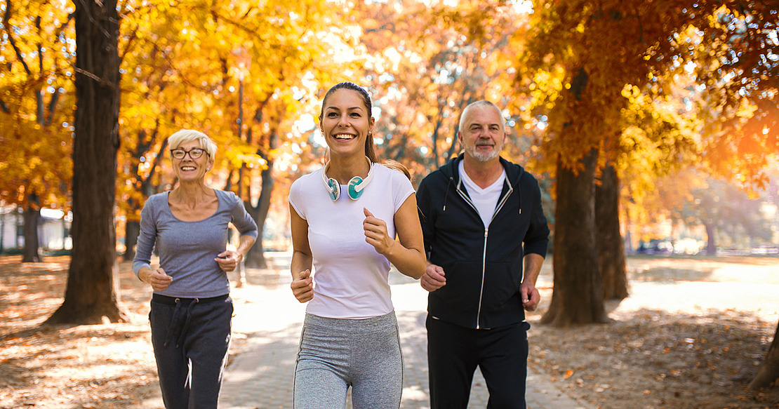 Ältere Frau, jüngere Frau und älterer Mann joggen im herbstlichen Park