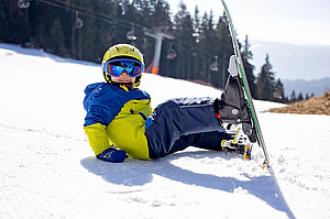 Kind mit Ski sitzt auf der Piste im Schnee