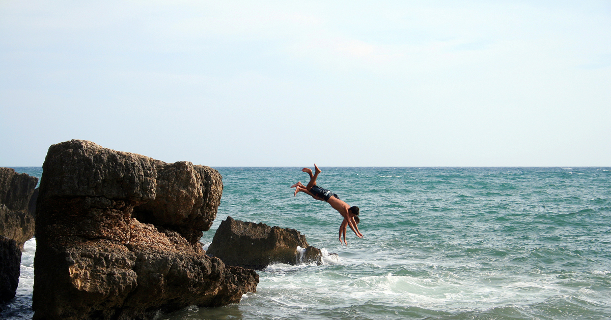 Zwei junge Männer springen kopfüber vom Felsen ns Meer